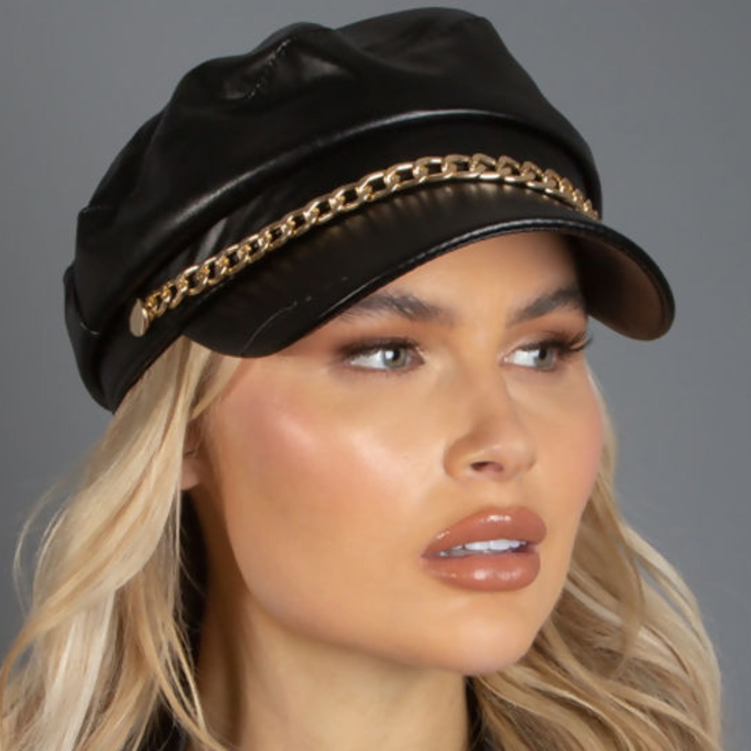 Model wears a black faux leather hat, with gold chain detailing.