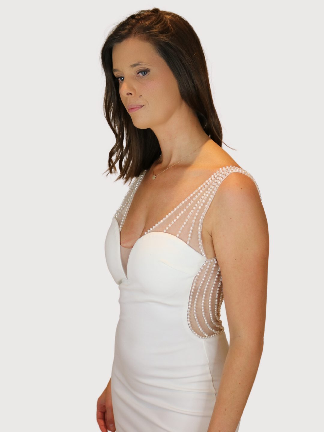 Model wears premium cream ini dress with low back pearl design and chunky gold zip detailing. The dress has a pearl detailing sttraps and a sweetheart neckline detailing. Model stands to the side. The front and side pearl panel detailing is visible.