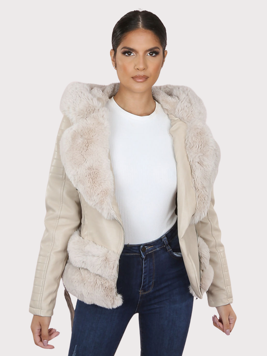 Female model stands in front of a plain background. The model wears a beige pu leather biker jacket with belted waist, zip front fastening and beige faux fur lapel and beige faux fur trim. The model faces the camera, the front of the jacket can be seen, including he faux fur trim at the base of the jacket.  The model has tanned skin and dark brown hair, she stands faces the camera with her jacket open and her hands by her sides. 