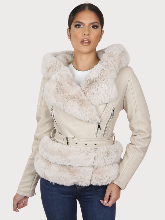 Female model stands in front of a plain background. The model wears a beige pu leather biker jacket with belted waist, zip front fastening and beige faux fur lapel and beige faux fur trim. The model faces the camera, the front of the jacket can be seen, including he faux fur trim at the base of the jacket.  The model has tanned skin and dark brown hair, she faces the camera and has one hand by her side and the other on her thighs. 