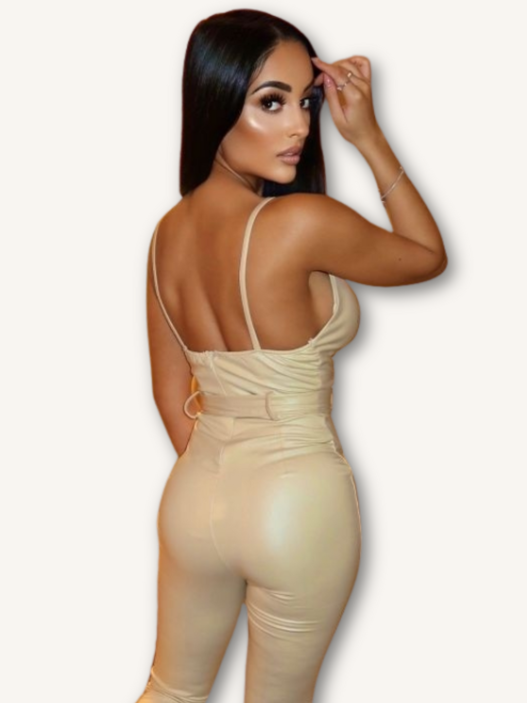 Model wears a beige faux leather jumpsuit with belted waist and plunging neckline. Model stands with her back to the camera. The back of her jumpsuit is visible and demonstrates the spaghetti straps and belted waist.