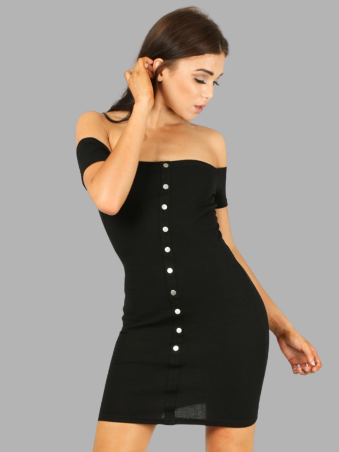 Female model stands in front of a plain grey background, she wears a black off the shoulder Bardot jersey mini dress, with front button detailing. The model has tanned skin and long brown hair, the model faces forward and  places one hand by her hair and the other by her side. The front of the dress can be seen, including the front button detailing. 