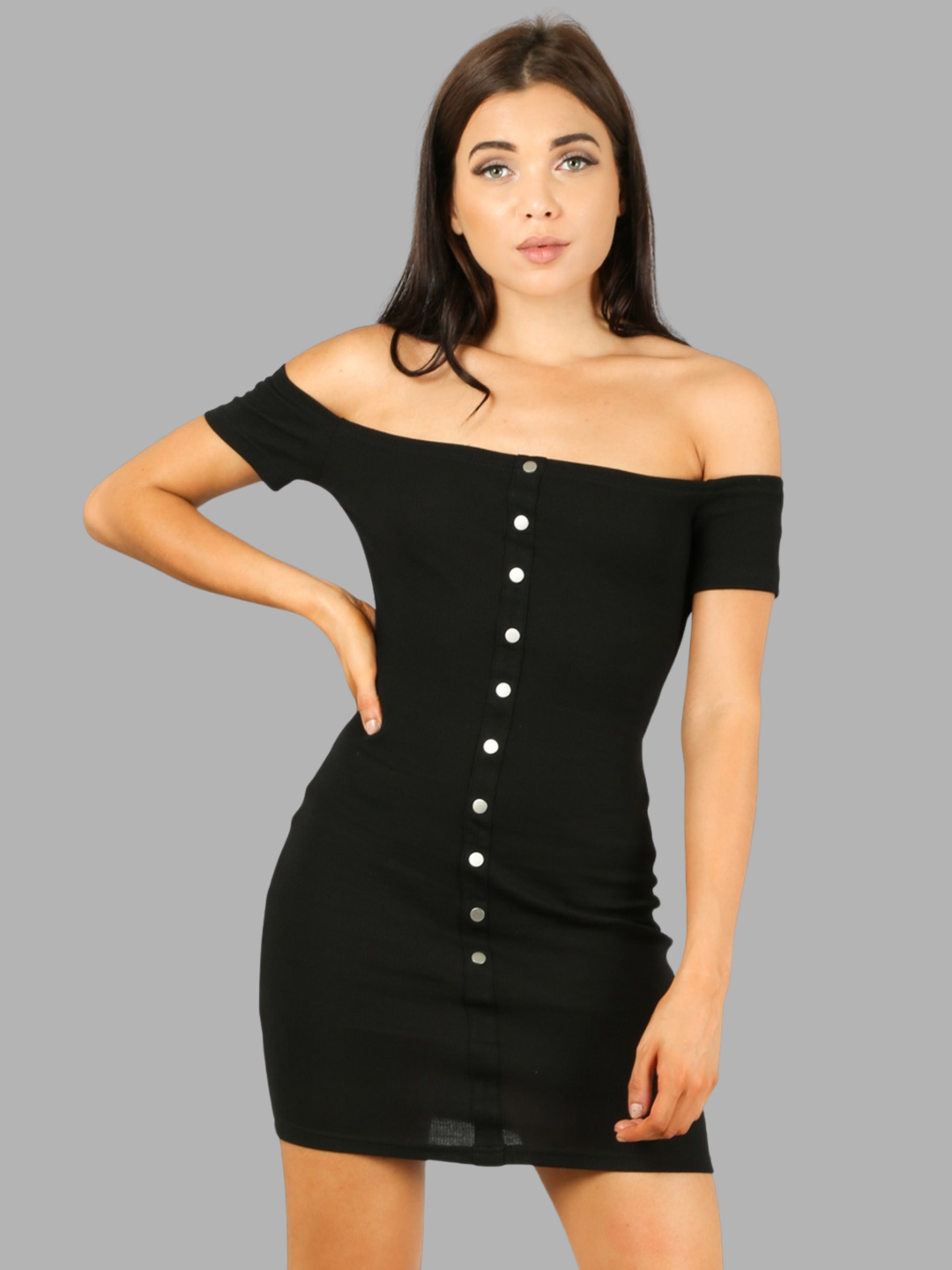 Female model stands in front of a plain grey background, she wears a black off the shoulder Bardot jersey mini dress, with front button detailing. The model has tanned skin and long brown hair, the model faces forward and has one hand on her hip and the other by her side. The front of the dress can be seen, including the front button detailing. 
