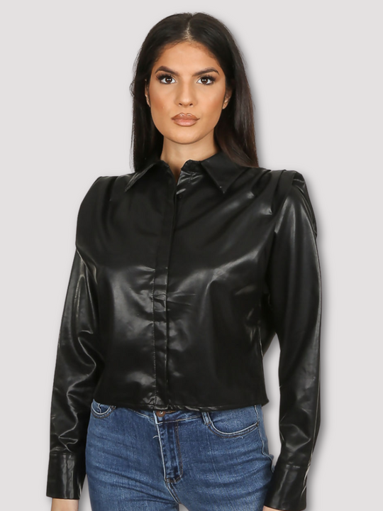 Model wears black faux leather shirt with pleated shoulders and long sleeve. The pu cropped front button shirt and collard neck. Model stands with her hands at her sides.