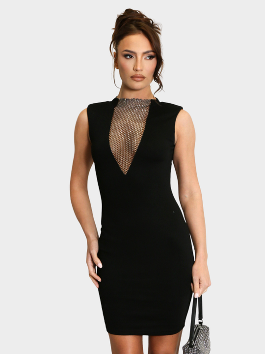 Model stands in front of a plain background, she wearsd a black sleeveless midi dress, with v neck diamante net design and bodycon fit. The model has tanned skin and brown hair that she has in a bun, she looks to the side and holds a diamante bag in one hand and places the other on her hip. 