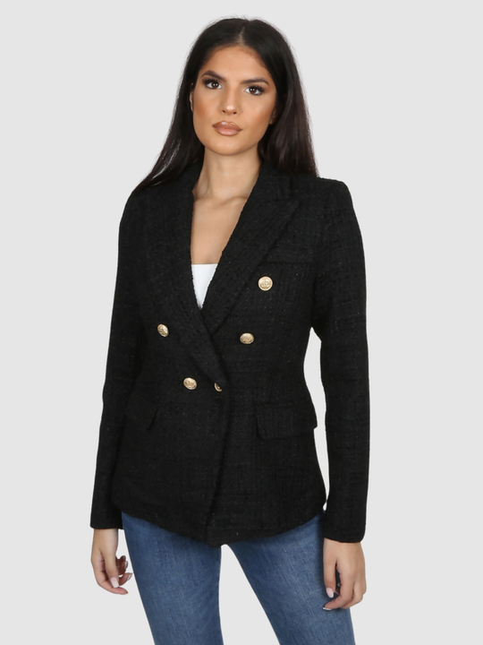 Model wears a black metallic yarn knitted double breasted blazer. The double breasted blazer has gold buttons at the front of the blazer and at the cuffs. Model faces forward with her hands by her sides.