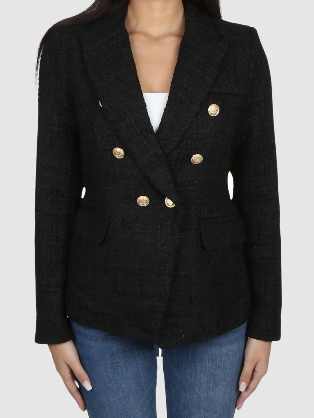 Model wears a black metallic yarn knitted double breasted blazer. The double breasted blazer has gold buttons at the front of the blazer and at the cuffs. She stands with her hands by her sides. 