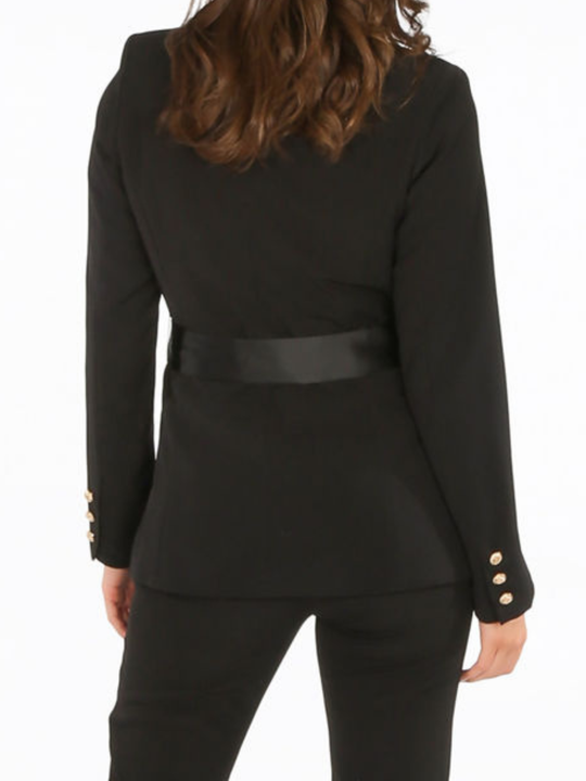 Close up. Model stands in front of a plain background. The model wears a luxe tailored black double breasted blazer, with  gold military button detailing and black satin lapel and black satin belt fastening. The back of the blazer can be seen, including the satin belt and gold military button cuffed sleeves.