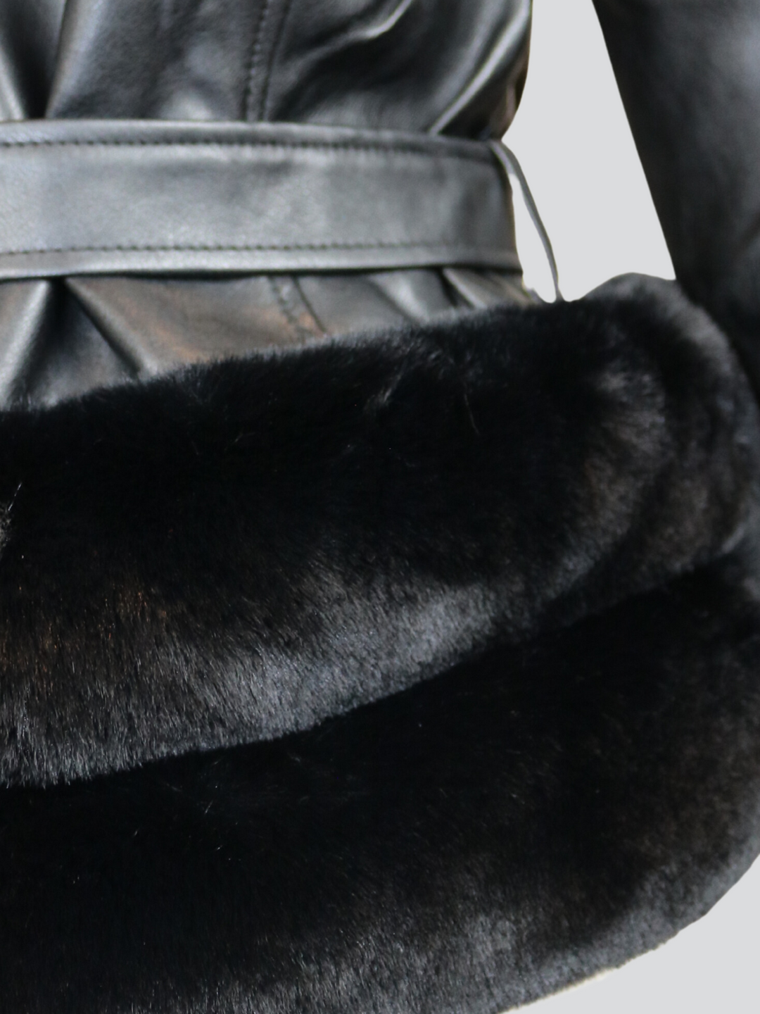 Close up shot. Ghost manequin wears a biker faux leather jacket with faux fur trim. The jacket has leather panelled detailing at the sleeves and exposed asymmetric chunky zip fastening. The faux leather jacket has a removable faux  belted waist.  Ghost manequin stands with their back to the camera, the  bottom part of the back of the jacket can be seen, including the faux fur trim and belted jacket.