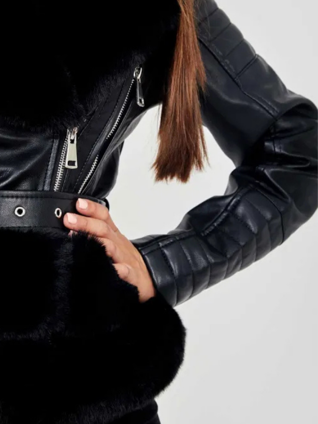 Ghost manequin wears a biker faux leather jacket with faux fur trim. The jacket has leather panelled detailing at the sleeves and exposed asymmetric chunky zip fastening. The faux leather jacket has a removable faux  belted waist.  Model stands with her hands on her hips, a close up of half the jacket can be seen. 