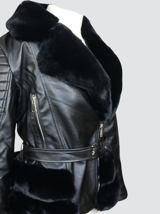 Ghost manequin wears a biker faux leather jacket with faux fur trim. The jacket has leather panelled detailing at the sleeves and exposed asymmetric chunky zip fastening. The faux leather jacket has a removable faux  belted waist.  The ghost manequin stands to the side. The side of the jacket can be seen. 
