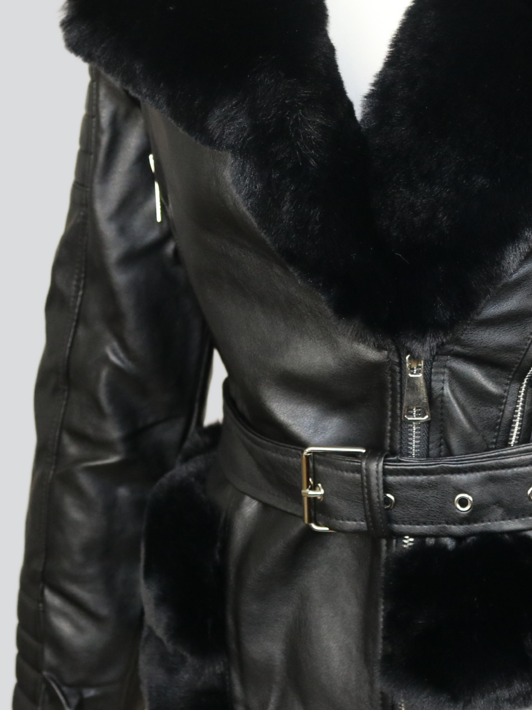 Ghost manequin wears a biker faux leather jacket with faux fur trim. The jacket has leather panelled detailing at the sleeves and exposed asymmetric chunky zip fastening. The faux leather jacket has a removable faux  belted waist.  A close up of the side of the trunk of jacket can be seen, including the faux fur trim at the bottom and faux fur lapel. 