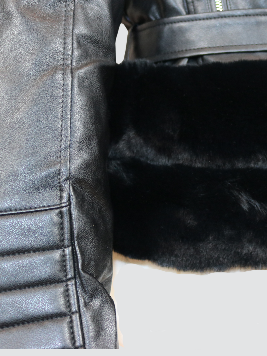 Ghost manequin wears a biker faux leather jacket with faux fur trim. The jacket has leather panelled detailing at the sleeves and exposed asymmetric chunky zip fastening. The faux leather jacket has a removable faux  belted waist.  A close up of the trunk of jacket can be seen, including a belted waist, faux fur trim and pannelled faux fur sleeves.