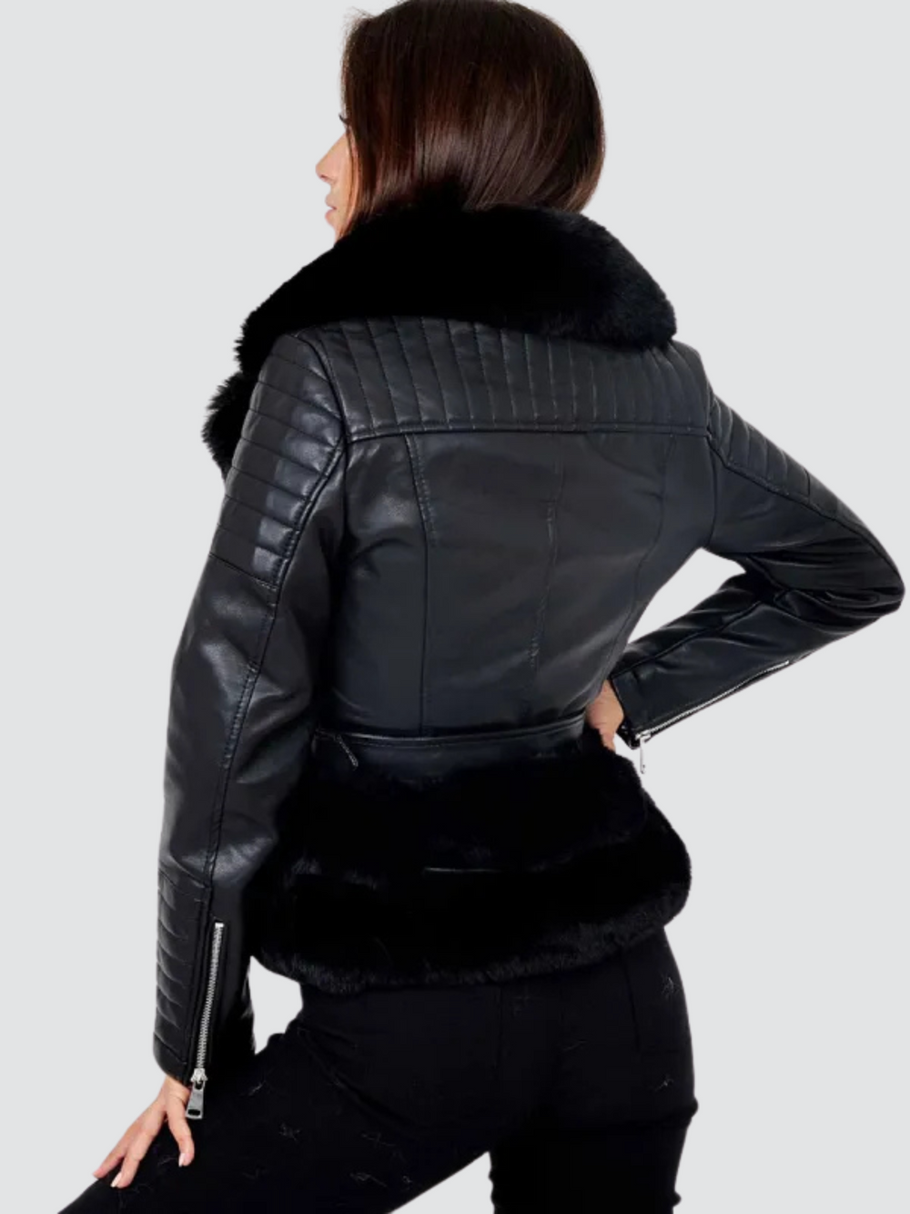 Model  wears a biker faux leather jacket with faux fur trim. The jacket has leather panelled detailing at the sleeves and exposed asymmetric chunky zip fastening. The faux leather jacket has a removable faux  belted waist. Model stands with her back to the camera. The back of the jacket can be seen including the top panelled detailing and the faux fur trim.