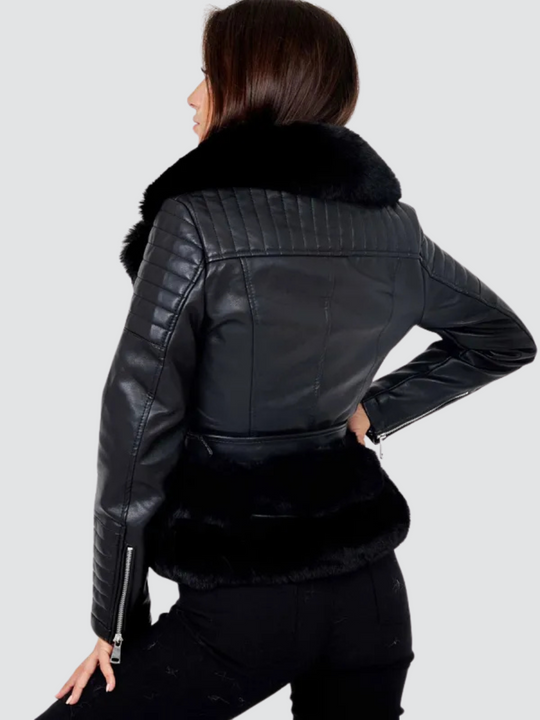 Model  wears a biker faux leather jacket with faux fur trim. The jacket has leather panelled detailing at the sleeves and exposed asymmetric chunky zip fastening. The faux leather jacket has a removable faux  belted waist. Model stands with her back to the camera. The back of the jacket can be seen including the top panelled detailing and the faux fur trim.