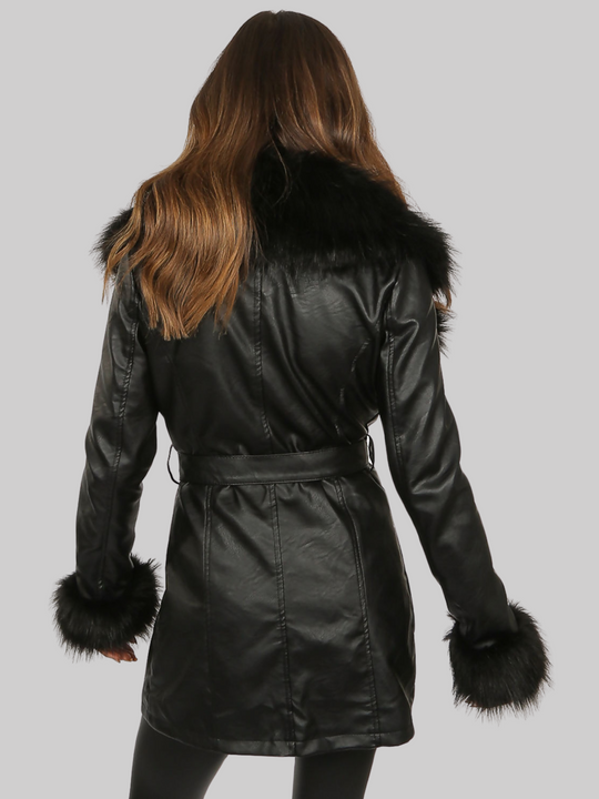 Model wears a black faux leather  coat with a longline silhouette. The coat has a faux fur ttrim and faux fur cuffs, there is a removable faux leather belt at the waist and side zip pockets.  Model stands with her back to the camera. The back of the faux leather coat cann be seen, including the waist and the large faux fur trim at the collar. 