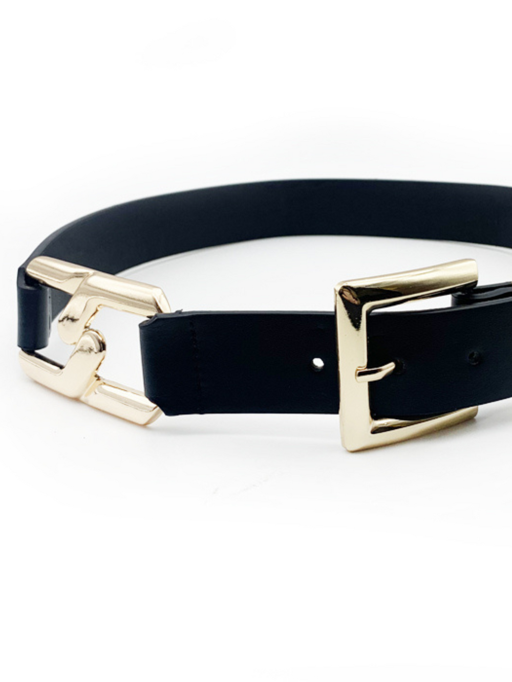 Close up of gold buckle. Black faux leather belt, with gold chain detailing and front gold buckle fastening. The belt has an adjustable waist ban and is placed on a plain cream background. 