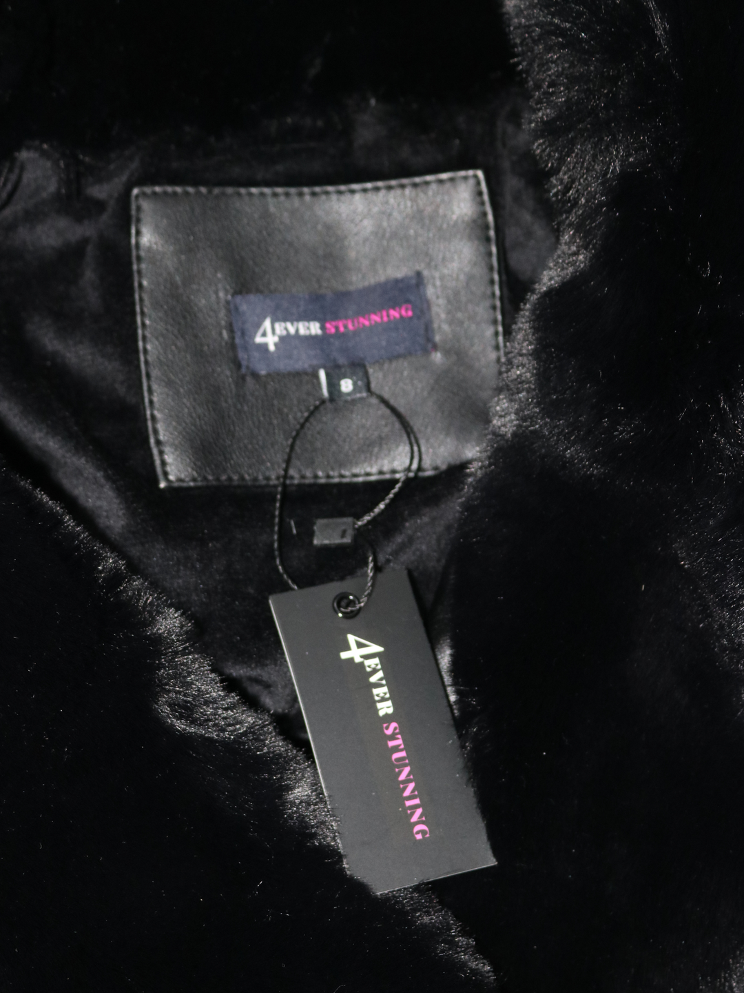 Closeup of the interior of the faux leather jacket with faux fur trim. The interior faux fur lining can be seen as well as the 4ever Stunning logo. 