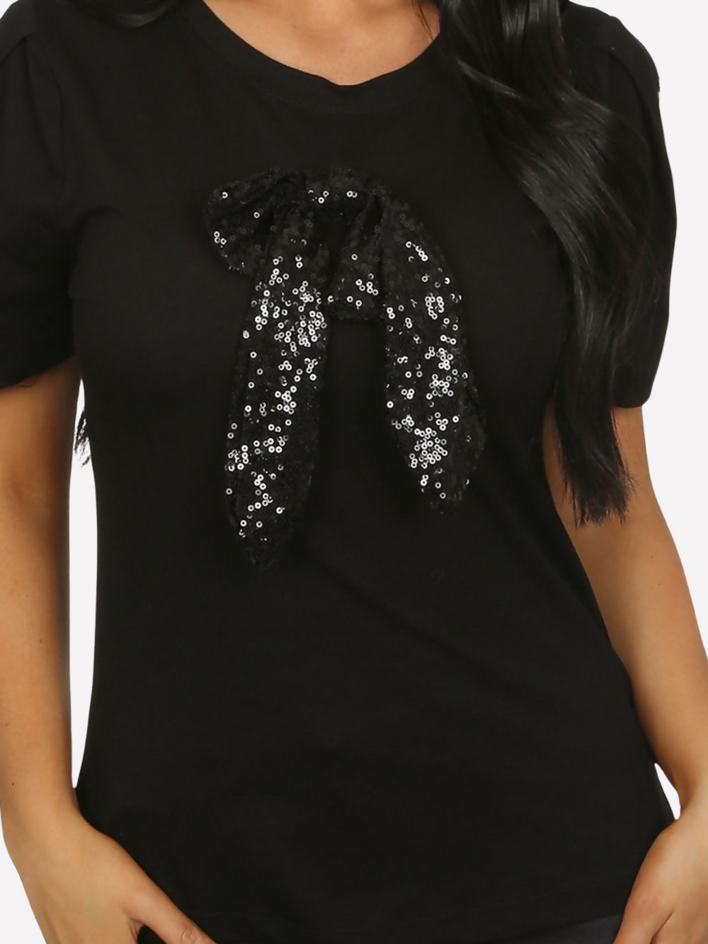 Close up shot. Female model wears a luxe black t shirt with a rounded neck amd 3/4 sleeves, with a large black sequin bow. 