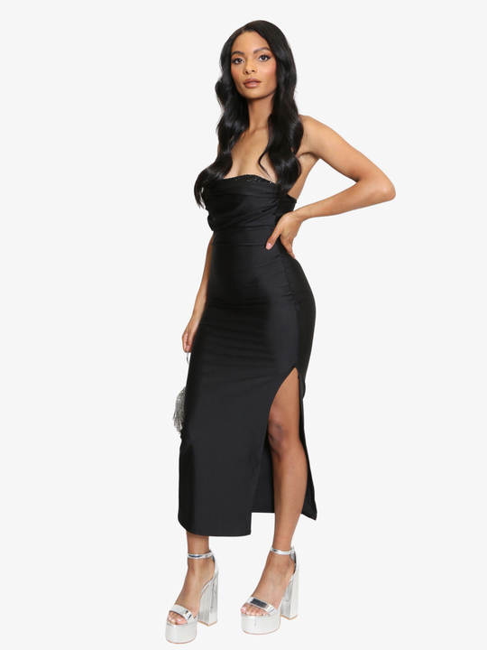 Full length shot. Female model stands in front of a plain background, she wears a black midi dress that has a ruched cup design and bandeau black sequin front insert. The midi dress also has a side split. The model has light brown skin and long black hair, she stands to the side, the thigh  high split can be seen, she wears silver platform heeled shoes. 