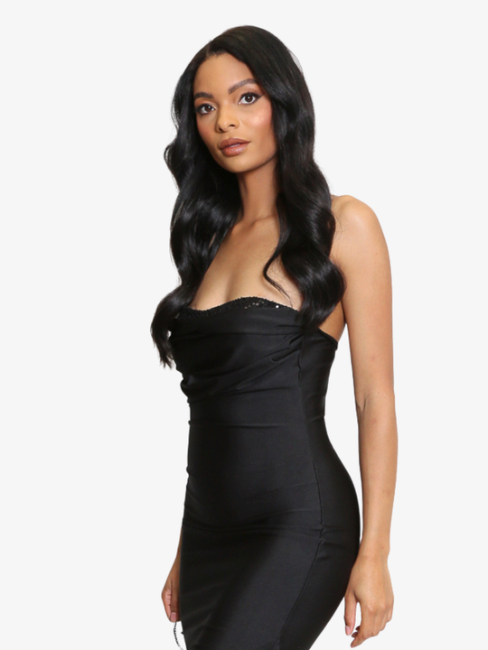 Female model stands in front of a plain background, she wears a black midi dress that has a ruched cup design and bandeau black sequin front insert. The midi dress also has a side split. The model has light brown skin and long black hair, she stands to the side and faces the camera, the side of teh maxi dress can be seen, as well as the top front bandeau sequin insert. 
