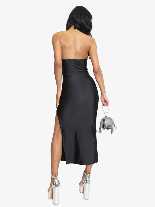 Female model stands in front of a plain background, she wears a black midi dress that has a ruched cup design and bandeau black sequin front insert. The midi dress also has a side split. The model has light brown skin and long black hair, she stands with her back to the camera, the side thigh split can be seen. 