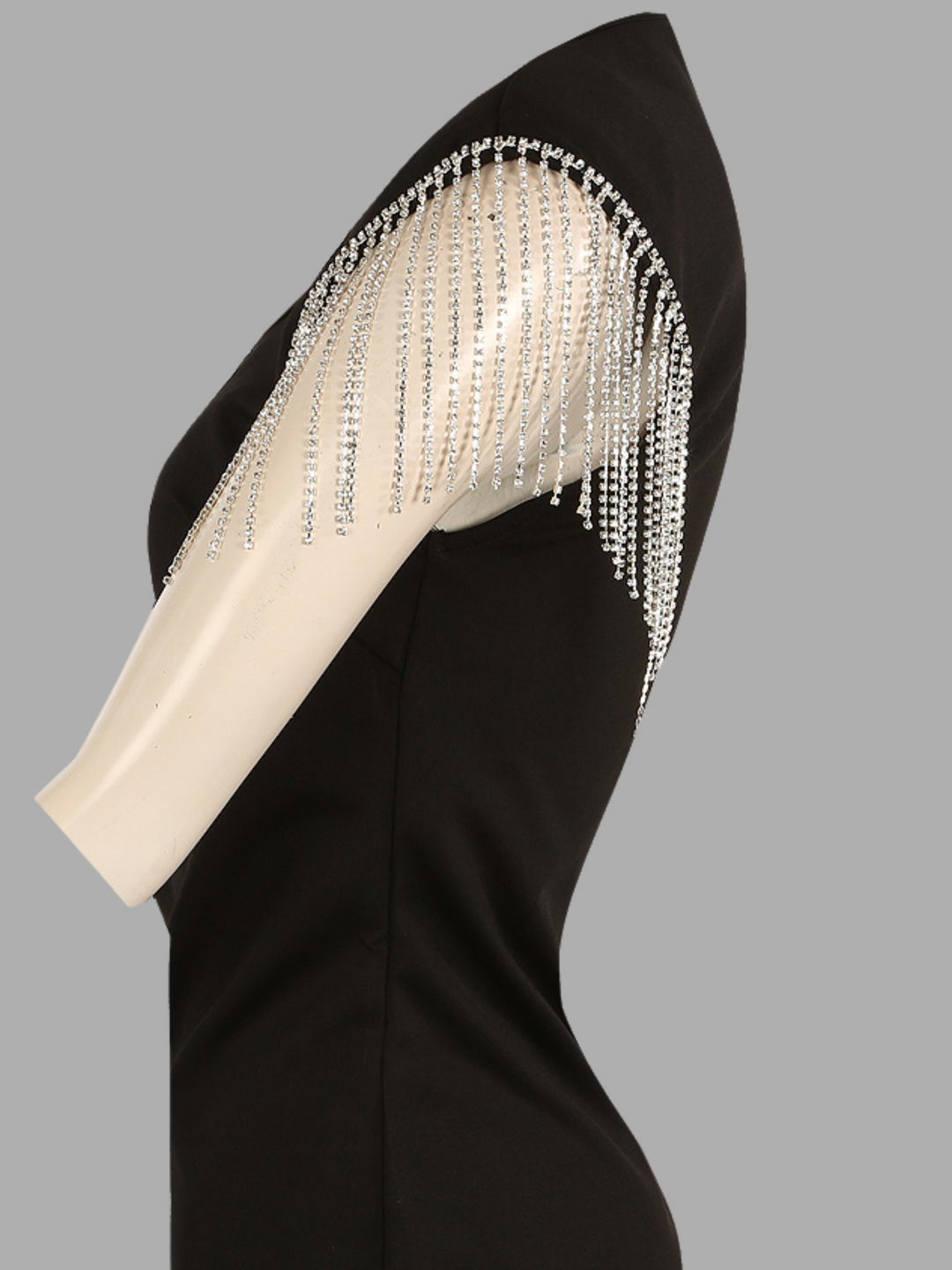 The ghost manequin wears luxe black mini dress with diamante tasseled sleeves.  The ghost manequin stands to the side, the side of the dress can be seen and the diamante tasseled sleeves are evident. 