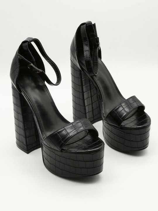 A croc chunky shoe is placed in front of a plain background. The model wears  a black platform shoe with chunky heels and adjustable ankle strap fastening.  The shoe is placed at a slight angle, the front and the side of the shoe can be seen. 