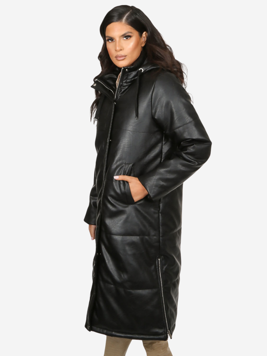 Model stands in front of a plain background, she wears a longline black faux leather quilted coat, with zip front and front button fastening.  The model has tanned skin and long dark brown hair, she stands to the side, the side of the coat can be seen, including the zipped sides and hooded draw string.