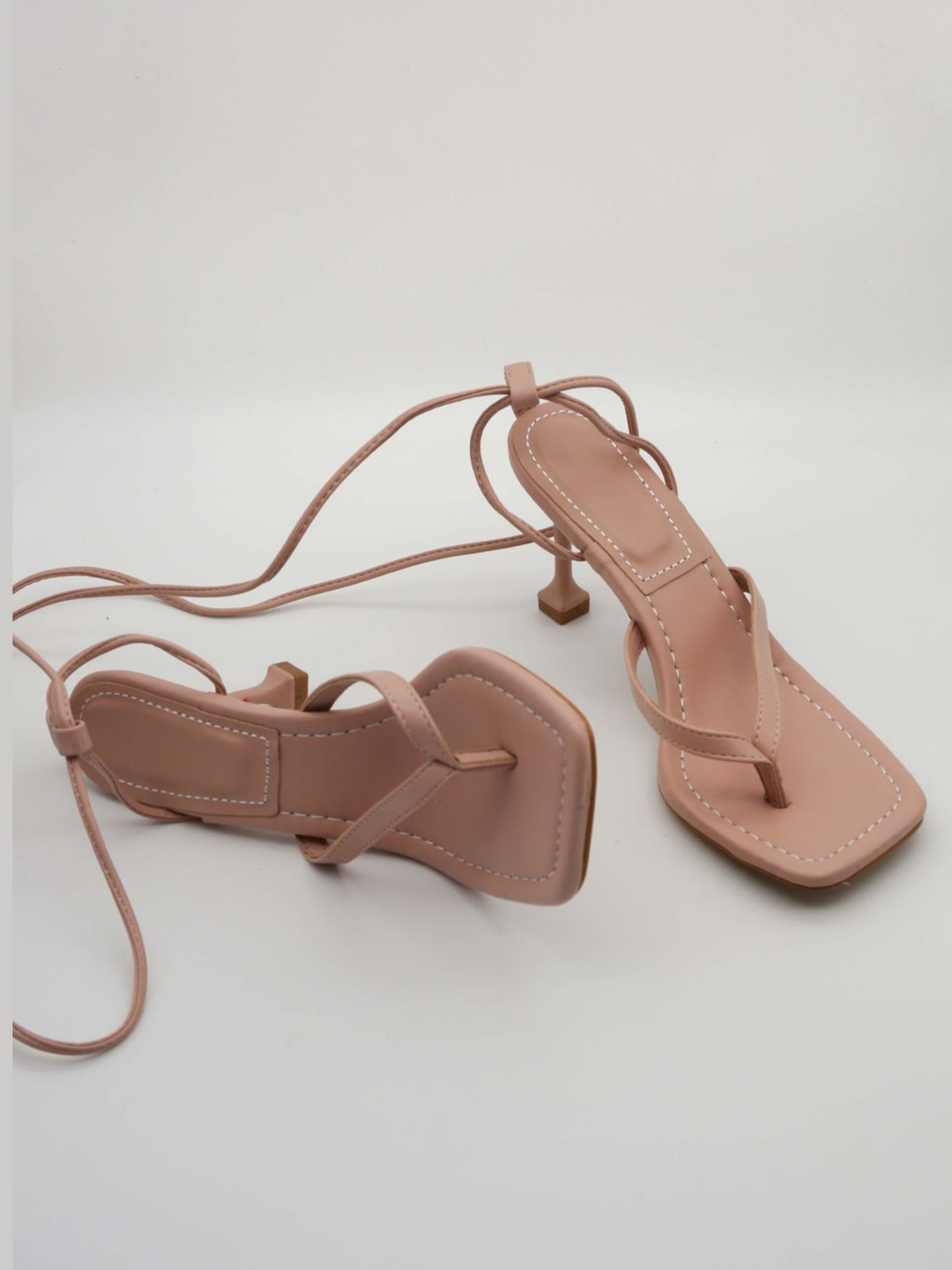 Lace up shoes can be seen on a plain background. The shoes has thong toe heeled shoe has a front design pu leather straps that are designed to lace up the leg. 