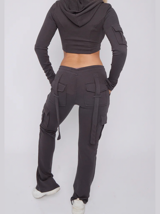 Torso and legs shot. Model wears a cropped top zip up  hoodie in  charcoal grey and matching drawstring joggers with a fitted cargo design. Model stands with her back to the camera, the loop back design of the cargo fitted joggers can be seen. The carfo sleeve of the hooded crop top is also visible. 
