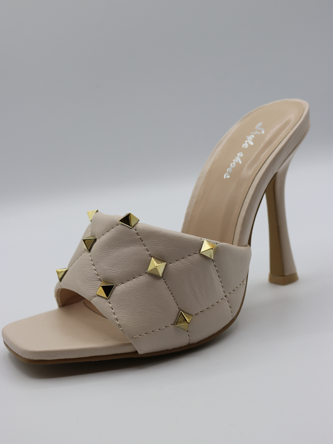 Cream quilted faux leather mule heels with gold studded heels. Photo shows the shoes from the side. The gold studded detailing is visible. 