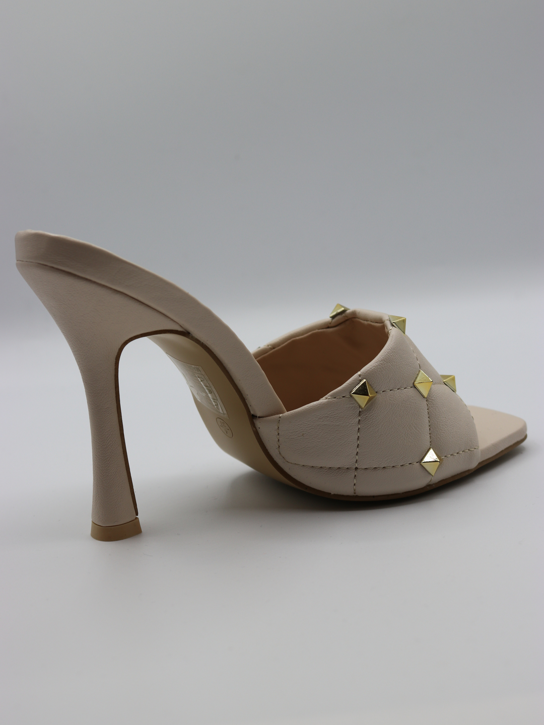Cream quilted faux leather mule heels with gold studded heels. The side of the shoe  is visible. 