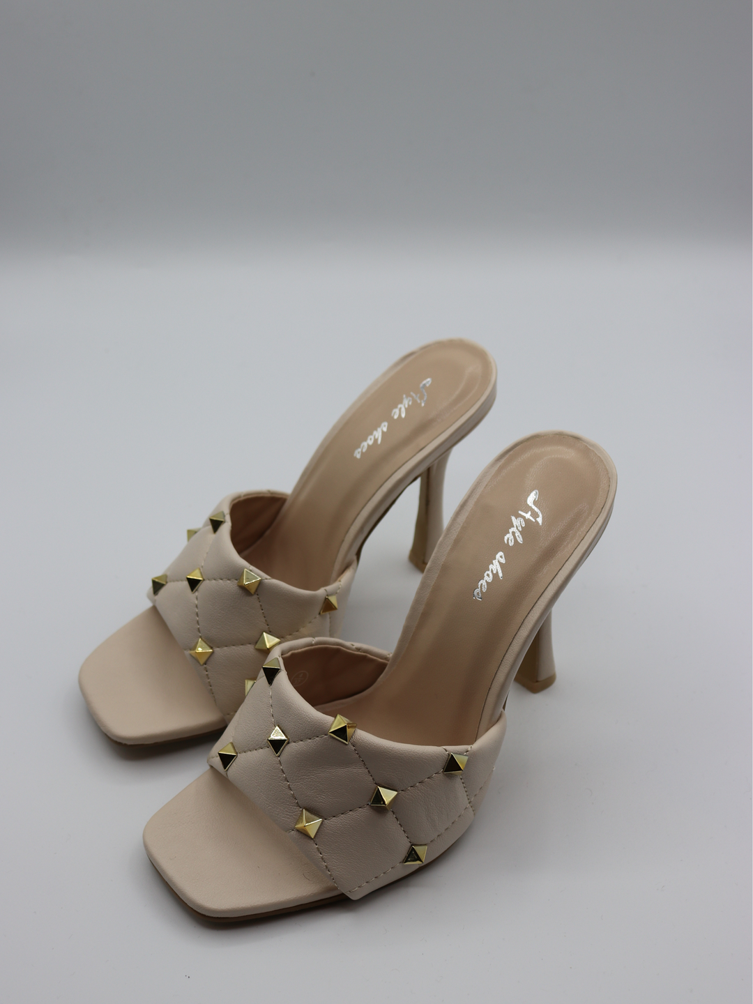 Cream quilted faux leather mule heels with gold studded heels. Photo shows the shoes from the side. The pair of shoes is visible. 