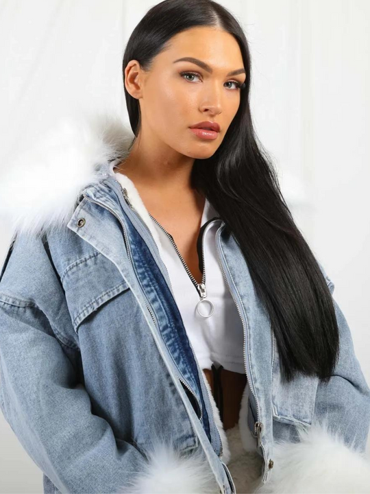 Model wears an oversized denim jacket with a white faux fur collar and white faux fur cuffs. Model looks into the camera with her dark hair swept to one side. 
