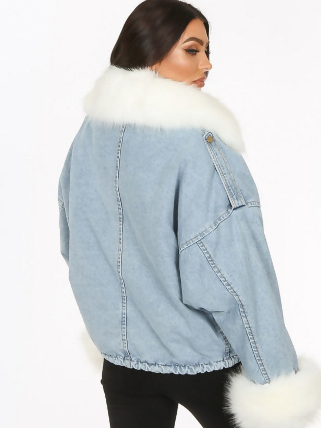 Model wears an oversized denim jacket with a white faux fur collar and white faux fur cuffs. Model stands with her back to the camera. The back of the jacket can be seen. 