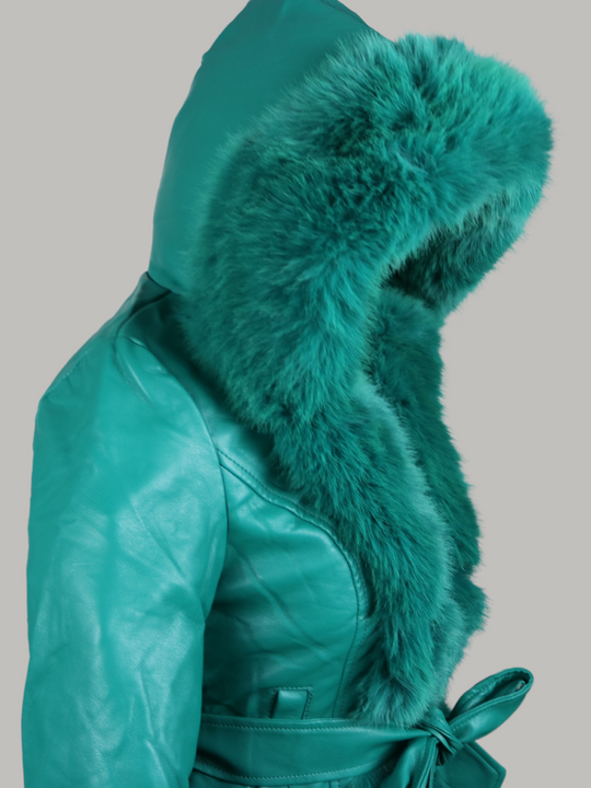 Ghost manequin wears a green faux leather jacket with green faux fur trim. The  green jacket has a faux fur hooded trim and large faux cuffs at the sleeves and a faux leather belt.  Ghost manequin stands to the side, wearing the faux fur hood on  and waering the removable faux belt.