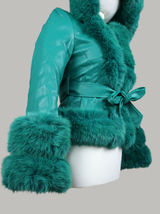 The manequin wears a green faux leather jacket with green faux fur trim. The  green jacket has a faux fur hooded trim and large faux cuffs at the sleeves and a faux leather belt.  The  manequin stands at an angle so that the large faux fur sleeves can be seen in focus. 
