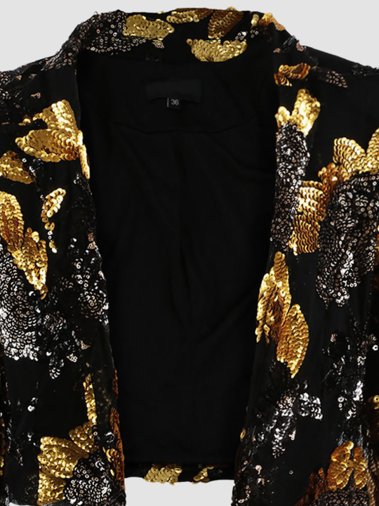Close up. Ghost mannequin stands in front of a plain background. The ghost mennequin wears a black and gold sequinned cropped blazer with open front and long sleeves.The black and gold sequinned blazer has an open front and a luxe design.  The close up shows a detailed black and gold sequinned design. 