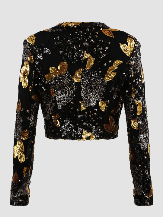 Ghost mannequin stands in front of a plain background. The ghost mennequin wears a black and gold sequinned cropped blazer with open front and long sleeves.The black and gold sequinned blazer has an open front and a luxe design. The ghost mannequin stands with his back to the camera, the back of the blazer can be seen, including the black and gold sequin design. 