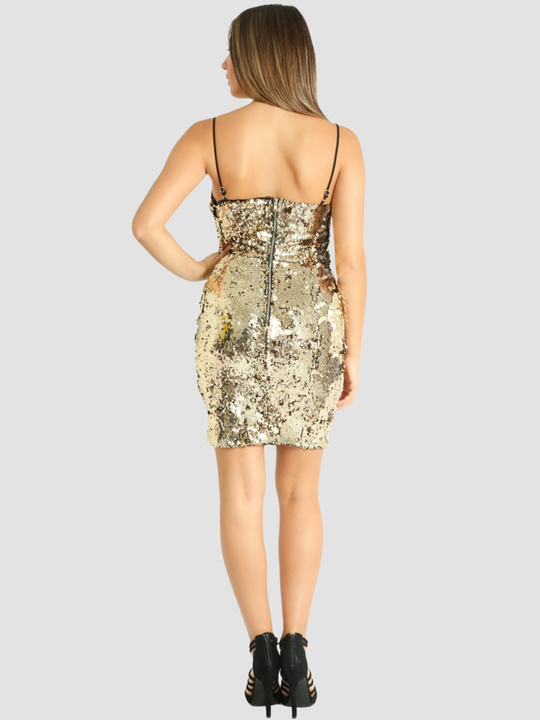 Full length shot. Female model stands in front of plain background. The model wears a gold sequin mini dress with a bodycon fit, a v neck design, black spaghetti shoulder straps and zip back fastening. The model has tanned skin and brown hair, she stands with her back to the camera, the back of the dress can be seen including the exposed zip back fastening and black spaghetti shoulder straps. The model wears high heeled shoes. 