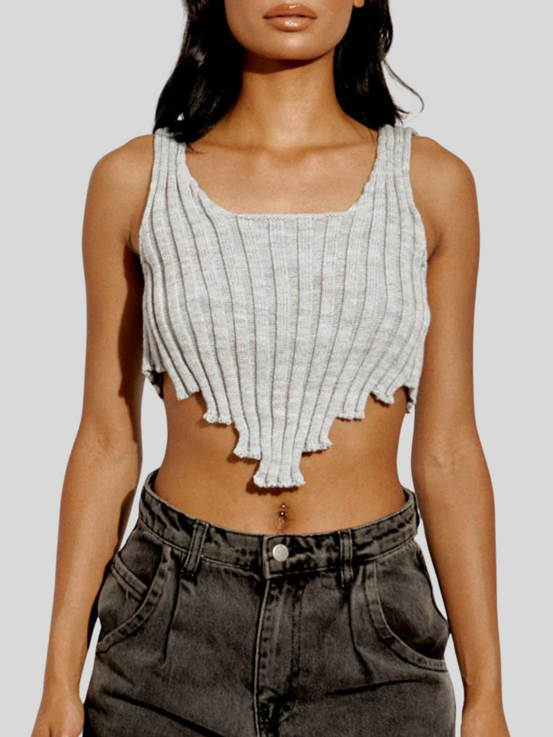 Close up. Model wears a grey knitted vest crop top with asymmetric hem trim. 