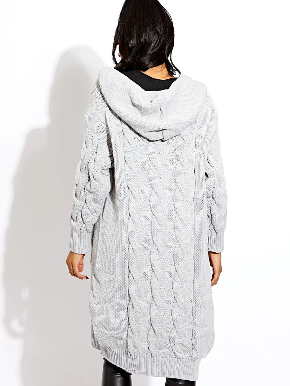 Female model stands in front of a plain background. The female model wears a long open cable knit Cardin in grey. The grey cable knit cardigan has long sleeves. The model has light brown skin and long black hair, she stands with her back to the camera with her hands by her sides. The hood of the cardigan can be seen. 