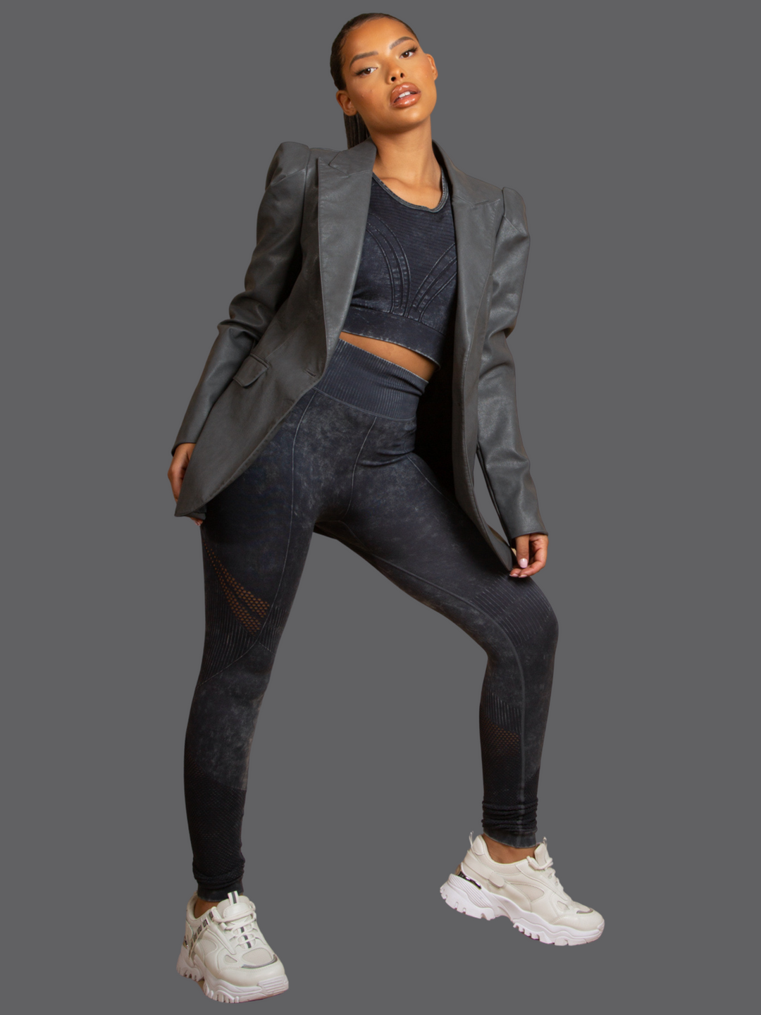 Full length shot Model wears of Grey Faux Leather Long Sleeved Blazer, With Front Pocket Look and Faux Leather Lapel. Model has light brown skin and a long pony tail. Model stands with one leg slightly bent and both hands by her sides.