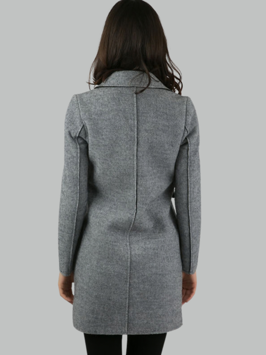 Female model stands in front of a plain background. The model wears a grey woolen coat with single front button fastening and grey tweed trim. The model has tanned skin and shoulder length hair, she stands with hher back to the camera, the back of the coat can be seen, including the exposed trim design.  