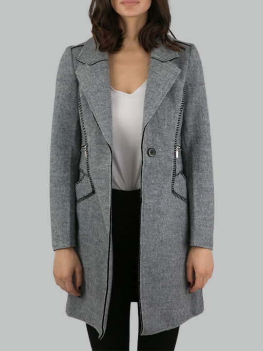 Close up. Female model stands in front of a plain background. The model wears a grey woolen coat with single front button fastening and grey tweed trim. The front of the grey knitted lapel and unbuttoned coat can be seen.