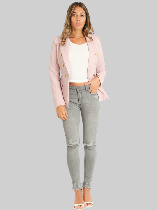 Full length shot. Female model wears a mauve double breatsted blazer with gold military buttons at the front of the blazer and the cuffs. The model has tanned skin and light brown hair,  she wears the double breasted blazer open and weras a white top, grey denim jeans and heels. 