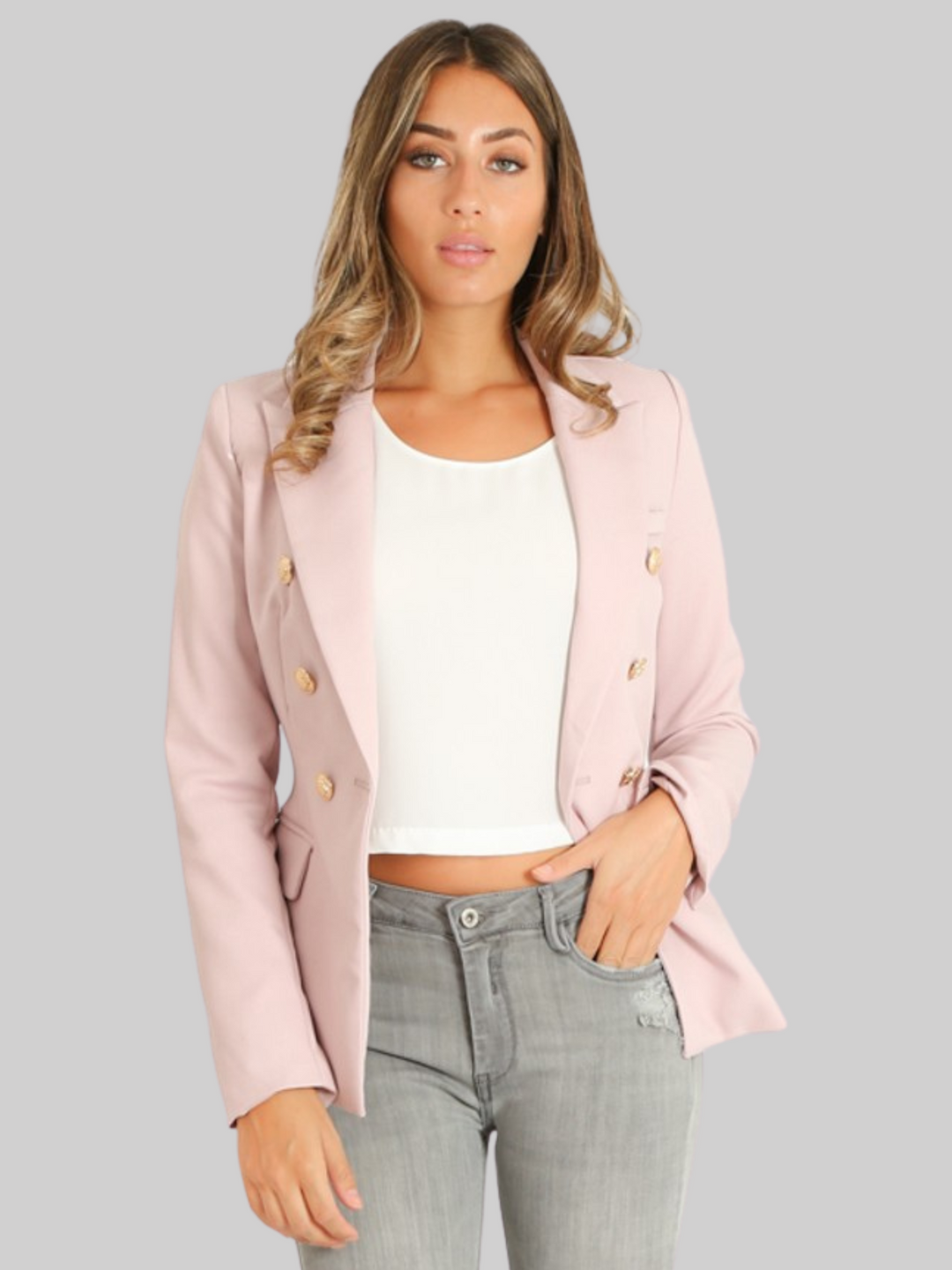 Female model wears a mauve double breatsted blazer with gold military buttons at the front of the blazer and the cuffs. The model has tanned skin and light brown hair, she wears the blazer open and places one hand in her jean pocket and the other by her side. 