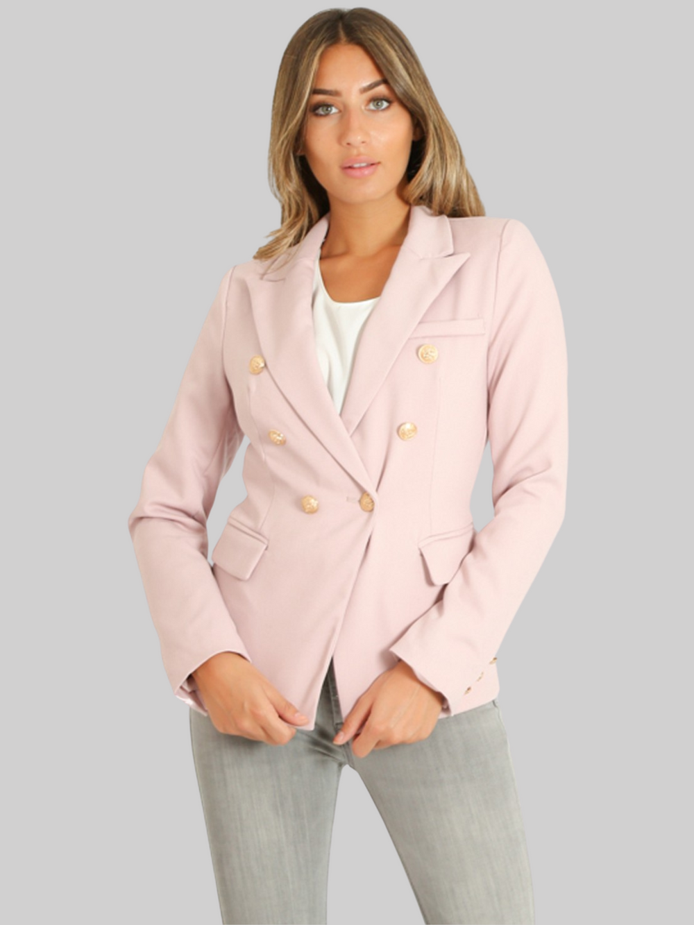 Female model wears a g double breatsted blazer with gold military buttons at the front of the blazer and the cuffs. The model has tanned skin and light brown hair, she faces the camera and has her hands in ffront of her.  She wears the double breasted blazer closed, the military gold button fastening can be seen. 