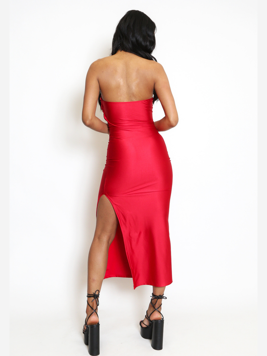 Full length shot. Female model stands in front of a plain background, she wears a red midi dress that has a ruched cup design and red bandeau sequin front insert. The midi dress also has a side split. The model has light brown skin and long black hair, she tands with her back to the camera, the back of the dress can be seen, including with a thigh side split. The model wears a black chunky heeled shoes.